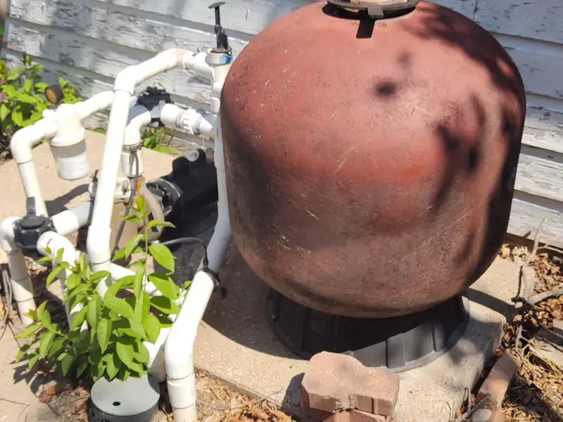 Rusted steel sand-filter tank on a cracked equipment pad, the kind of end-of-life equipment a buyer should price before closing